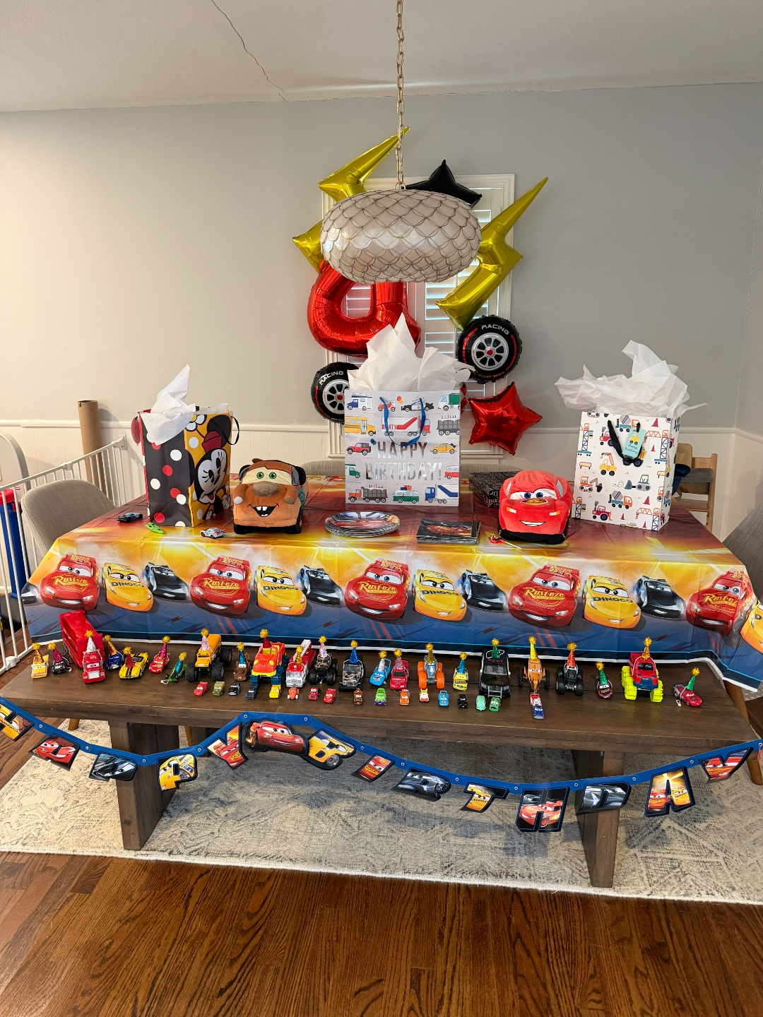 Cars Lightning McQueen 4th birthday party table with full die-cast car collection lined up on bench and foil lightning bolt balloons overhead