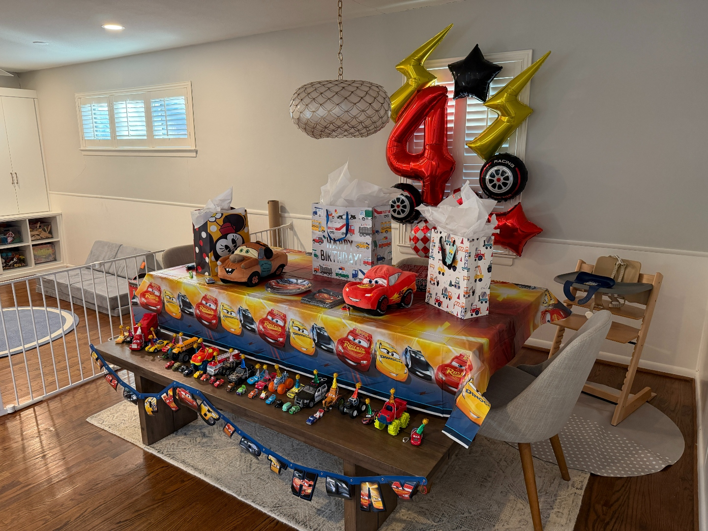 Wide angle of Cars birthday party setup with number 4 foil balloon, Mater plush, Lightning McQueen pillow, and Cars banner on bench