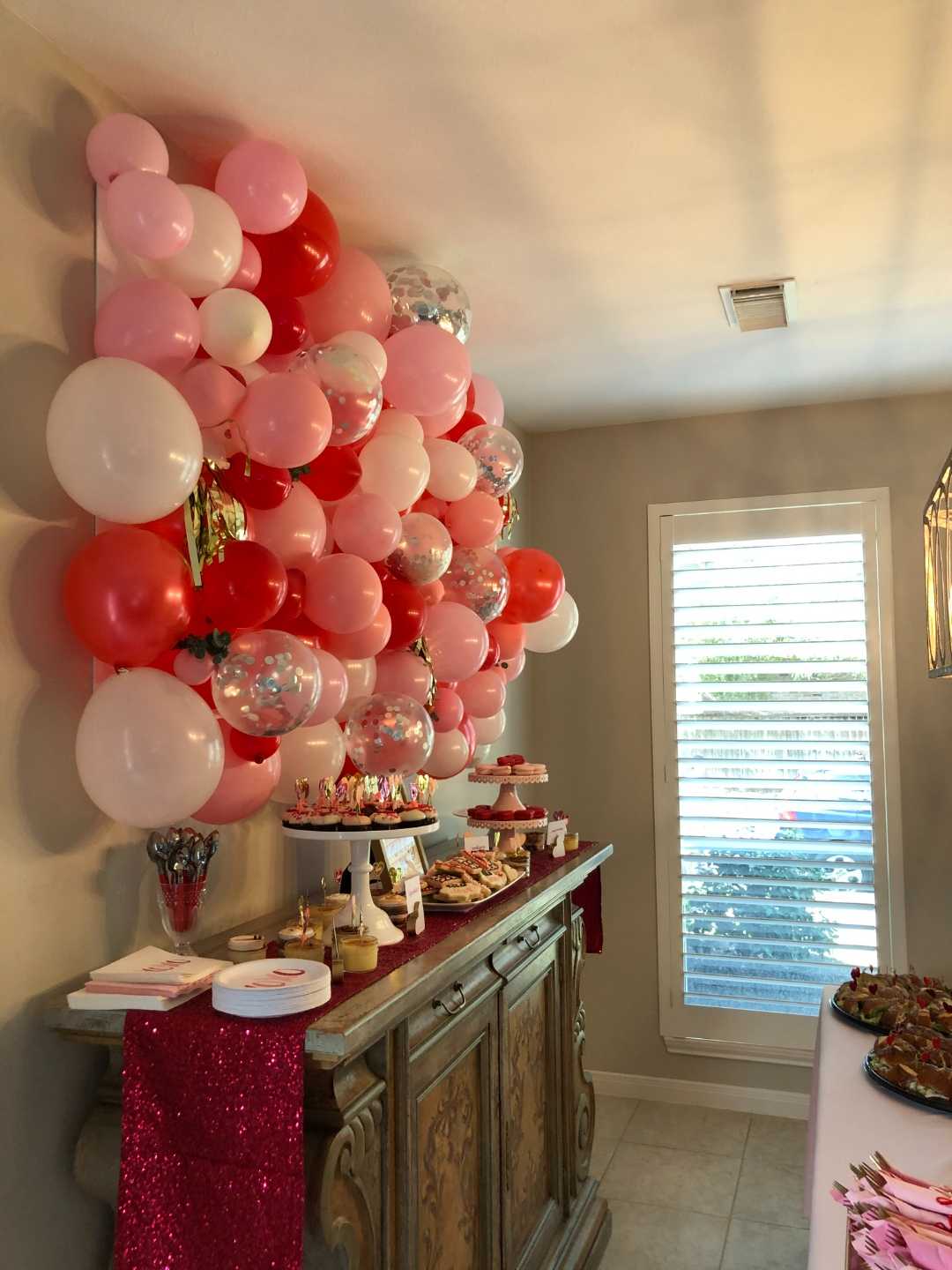 Full view of balloon wall and dessert table with crimson glitter runner and tiered cake stands